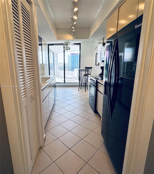 kitchen with ceiling fan, electric range oven, black fridge, track lighting, and light tile patterned floors