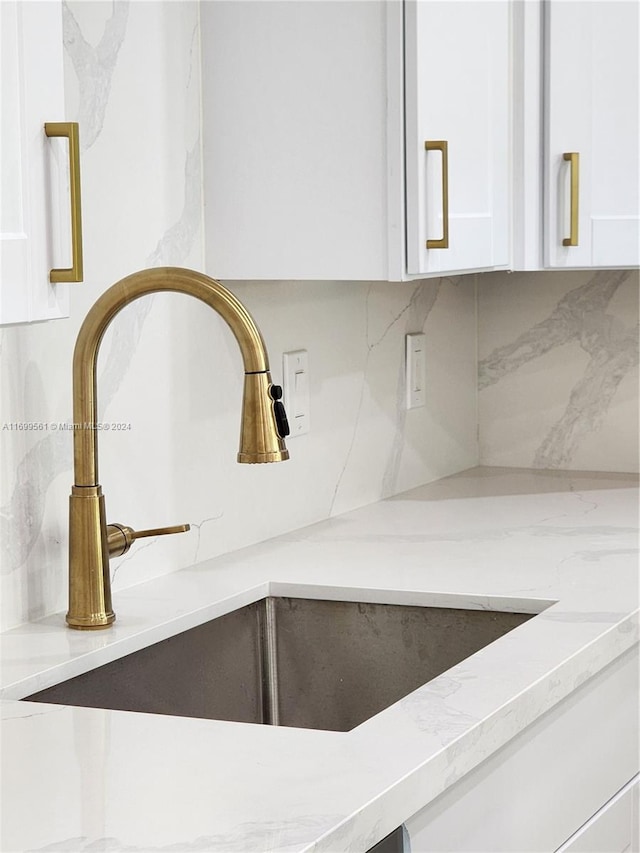 interior details featuring decorative backsplash, sink, white cabinets, and light stone countertops