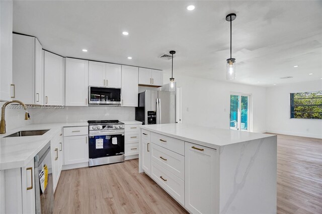 kitchen featuring appliances with stainless steel finishes, sink, light hardwood / wood-style floors, white cabinetry, and hanging light fixtures