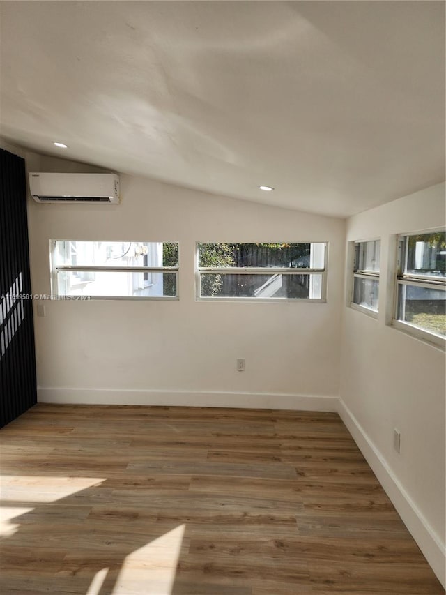 unfurnished room with a wall mounted AC, plenty of natural light, wood-type flooring, and lofted ceiling