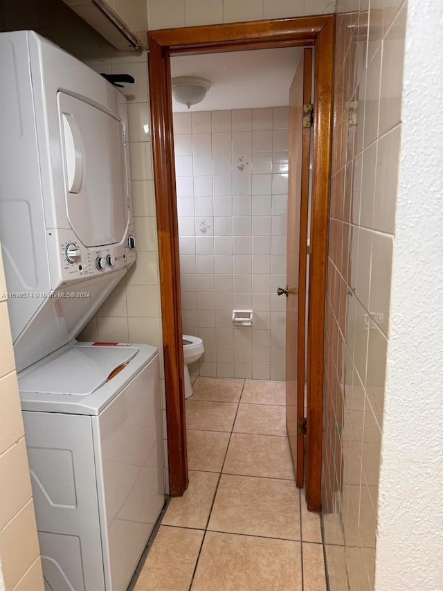 laundry area with stacked washer / dryer, light tile patterned floors, and tile walls