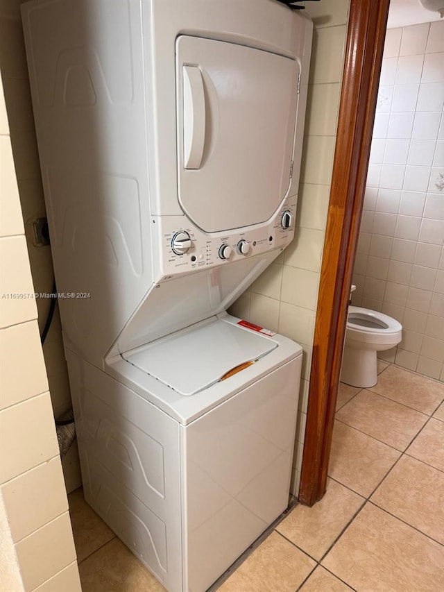 washroom with stacked washing maching and dryer, tile walls, and light tile patterned floors