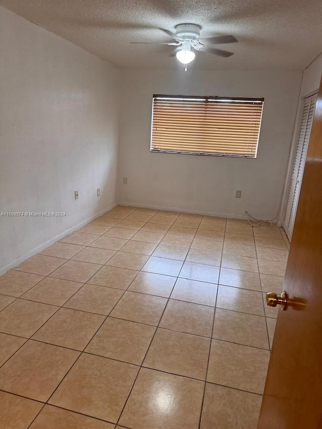 spare room featuring ceiling fan, light tile patterned floors, and a textured ceiling