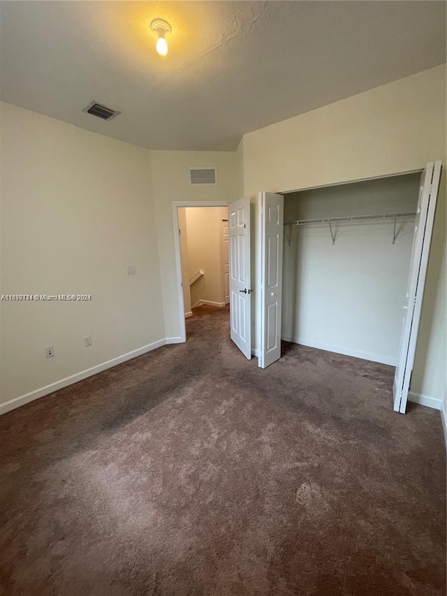 unfurnished bedroom with dark carpet and a closet