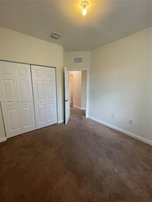 unfurnished bedroom with dark carpet and a closet