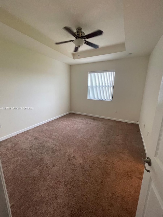 unfurnished room featuring a tray ceiling, dark carpet, and ceiling fan