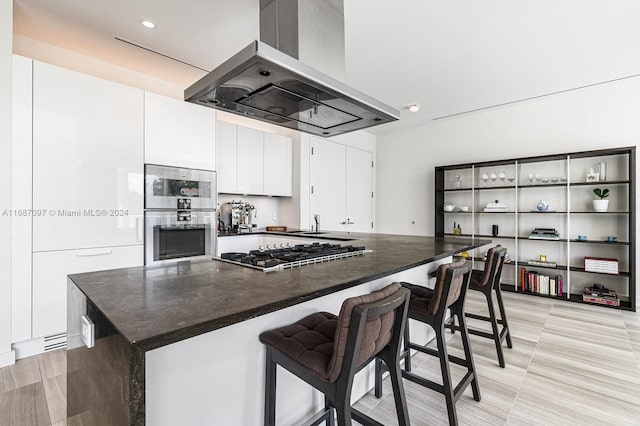 kitchen featuring island exhaust hood, appliances with stainless steel finishes, a spacious island, white cabinets, and a breakfast bar area