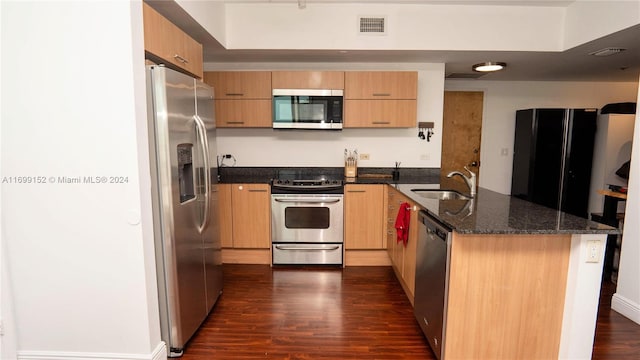 kitchen with kitchen peninsula, dark stone counters, stainless steel appliances, dark wood-type flooring, and sink