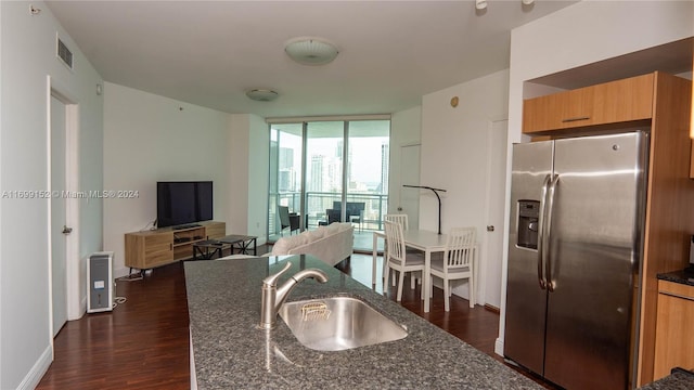 kitchen with dark stone counters, sink, dark hardwood / wood-style floors, stainless steel fridge, and a wall of windows