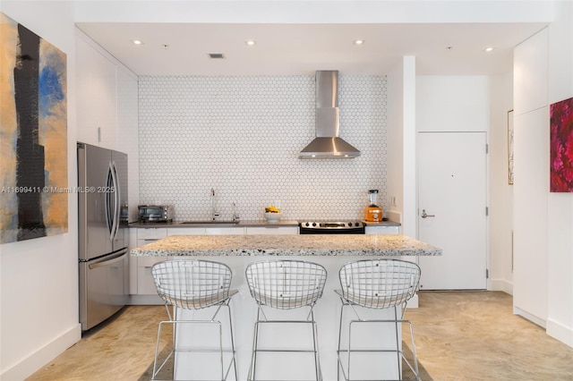 kitchen with tasteful backsplash, a kitchen island, wall chimney exhaust hood, and appliances with stainless steel finishes