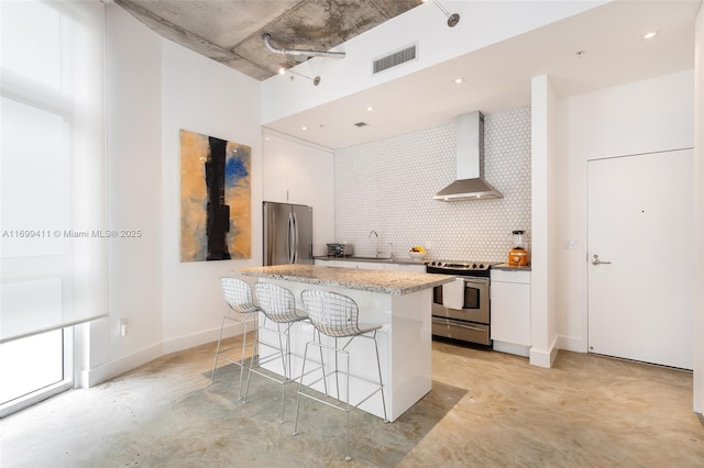 kitchen with a center island, wall chimney exhaust hood, stainless steel appliances, a kitchen bar, and white cabinets