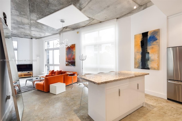 kitchen with finished concrete flooring, stainless steel fridge, light stone counters, and white cabinets