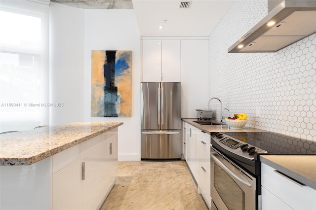 kitchen with visible vents, appliances with stainless steel finishes, white cabinets, a sink, and wall chimney range hood