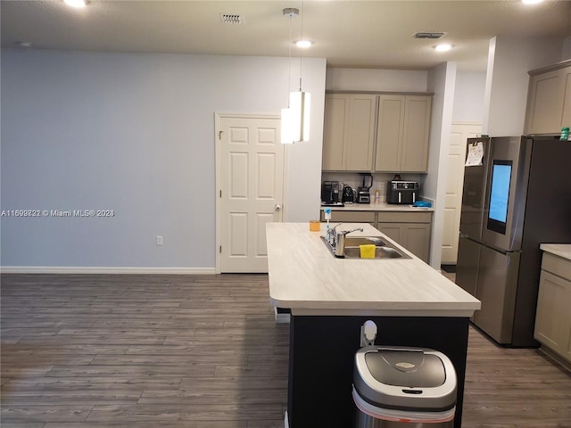 kitchen with sink, dark wood-type flooring, stainless steel fridge, an island with sink, and decorative light fixtures