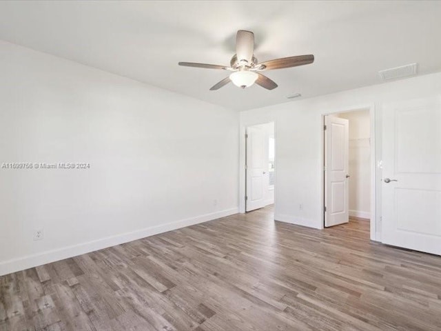 unfurnished bedroom featuring light wood-type flooring, a walk in closet, a closet, and ceiling fan