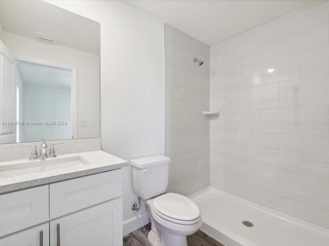 bathroom featuring wood-type flooring, vanity, a tile shower, and toilet