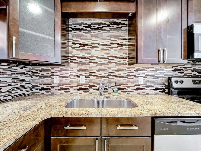 kitchen featuring dark brown cabinetry, sink, tasteful backsplash, light stone counters, and appliances with stainless steel finishes