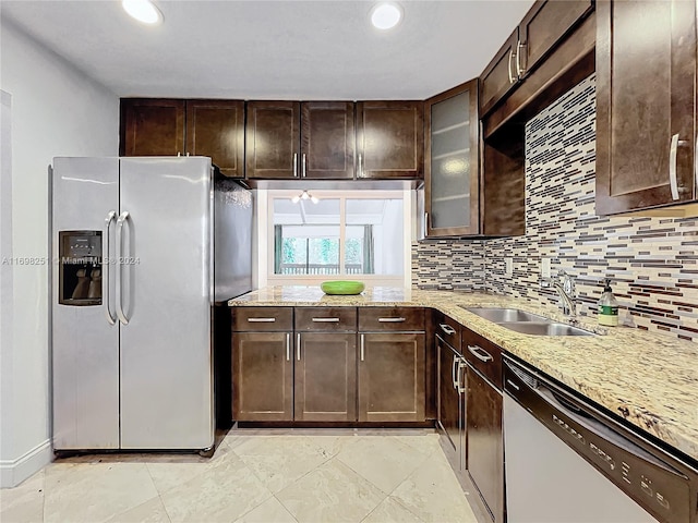 kitchen featuring sink, stainless steel appliances, tasteful backsplash, light stone counters, and dark brown cabinets