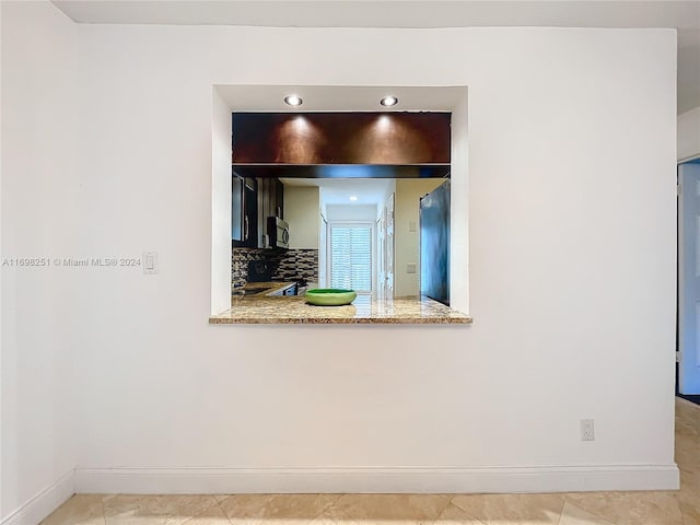 kitchen with decorative backsplash, light tile patterned floors, light stone counters, and fridge