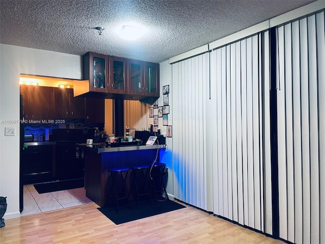 kitchen with a breakfast bar, a textured ceiling, light wood-type flooring, and kitchen peninsula