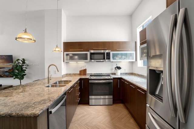 kitchen with appliances with stainless steel finishes, sink, hanging light fixtures, light stone counters, and kitchen peninsula