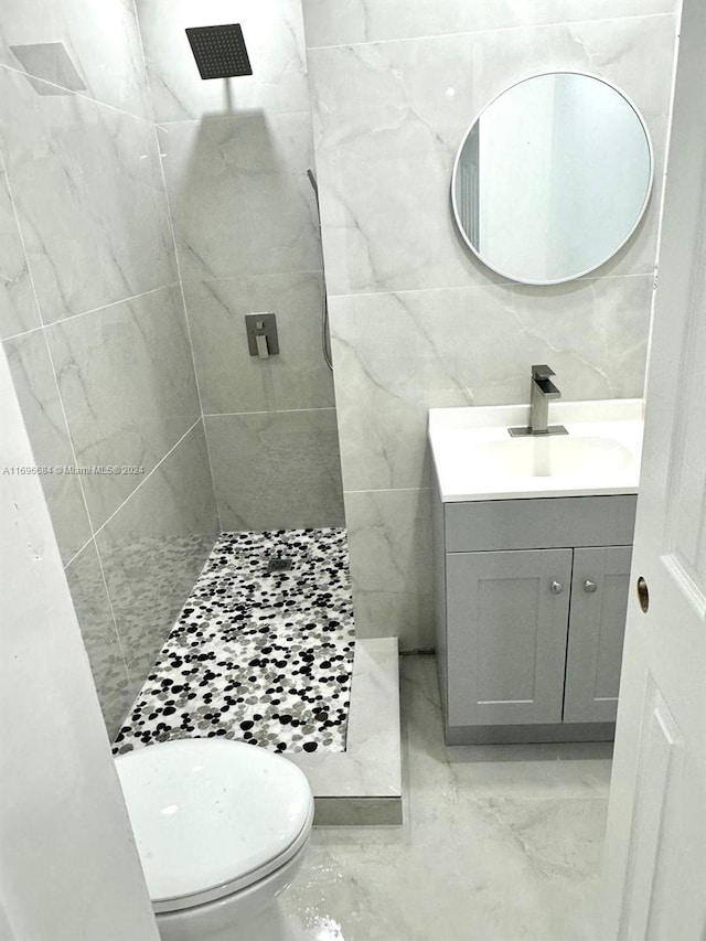 bathroom featuring tiled shower, vanity, toilet, and tile walls