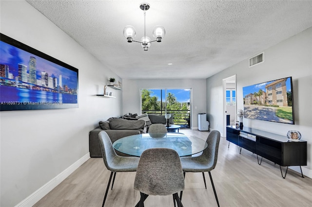 dining area with a textured ceiling, light hardwood / wood-style flooring, and a notable chandelier