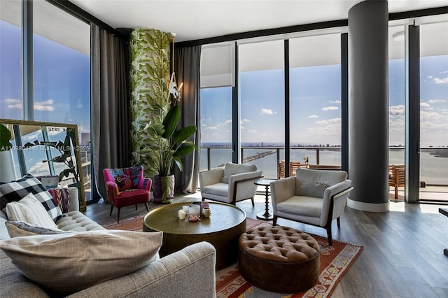 living room featuring hardwood / wood-style flooring, decorative columns, floor to ceiling windows, and a water view