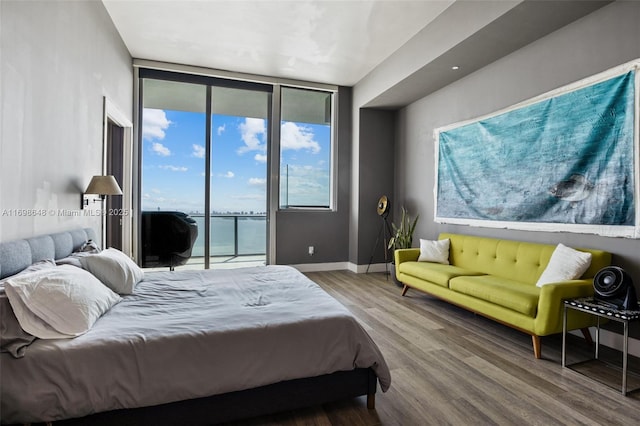 bedroom featuring multiple windows, floor to ceiling windows, a water view, and access to outside