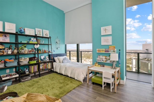 bedroom with hardwood / wood-style flooring, a towering ceiling, floor to ceiling windows, and multiple windows