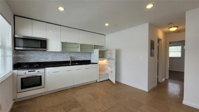 kitchen with tasteful backsplash, sink, oven, electric panel, and white cabinetry