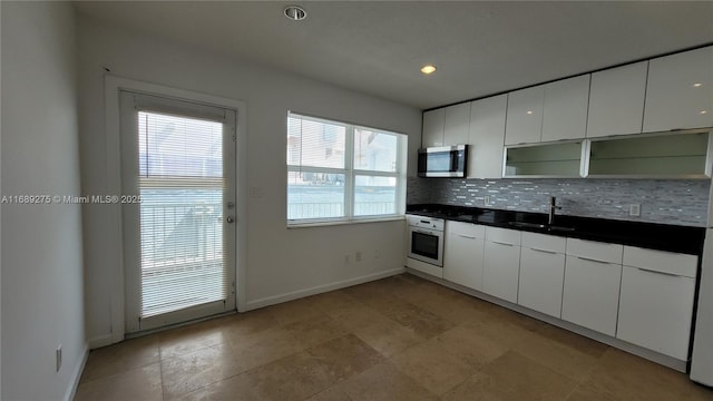 kitchen featuring oven, white cabinetry, sink, and a wealth of natural light