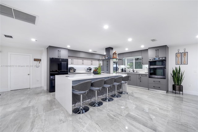 kitchen featuring a kitchen breakfast bar, double oven, sink, gray cabinets, and a kitchen island