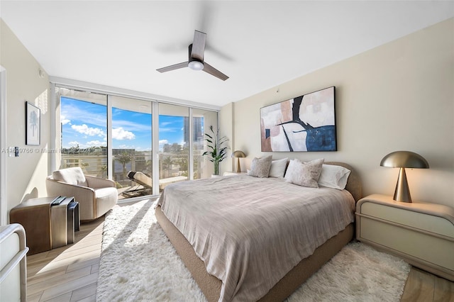 bedroom with access to outside, ceiling fan, expansive windows, and light hardwood / wood-style floors