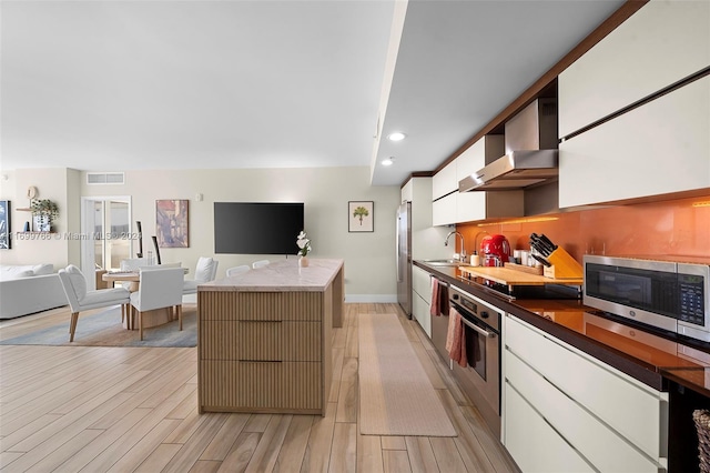 kitchen featuring white cabinetry, light hardwood / wood-style floors, wall chimney range hood, and appliances with stainless steel finishes