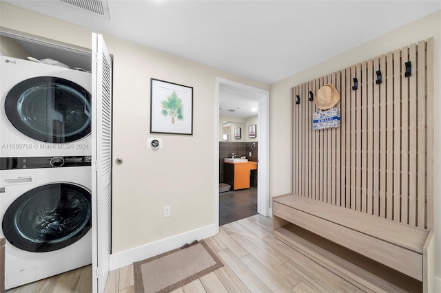 laundry area with light hardwood / wood-style flooring and stacked washer / drying machine