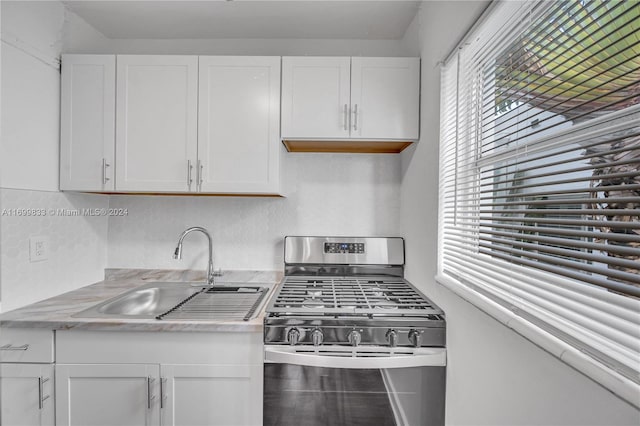 kitchen featuring sink, backsplash, white cabinetry, and stainless steel gas range