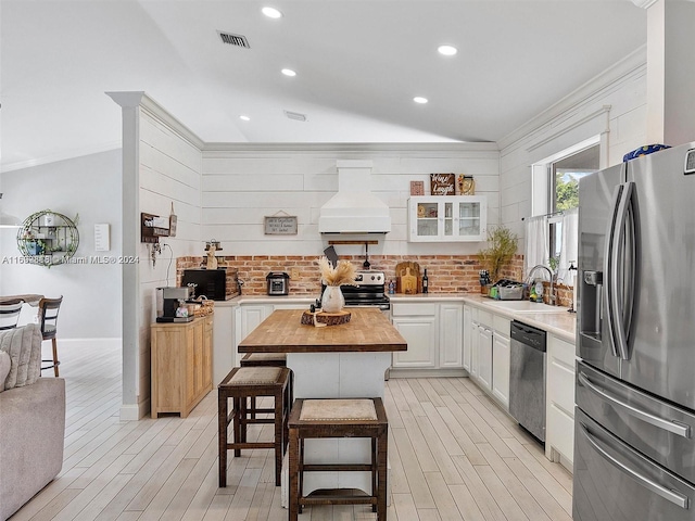 kitchen featuring butcher block counters, white cabinetry, sink, premium range hood, and appliances with stainless steel finishes