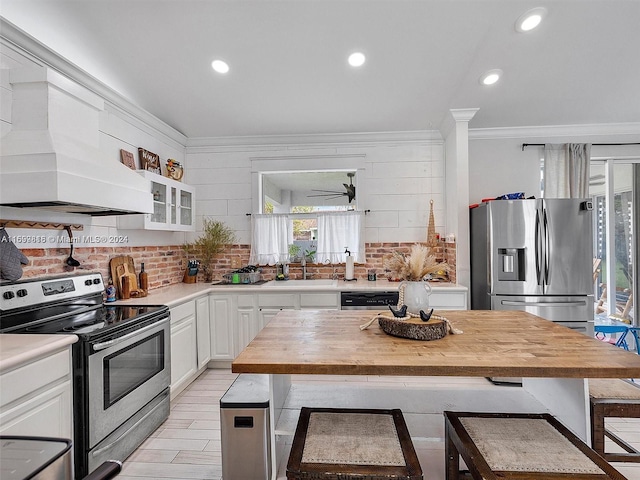 kitchen featuring wood counters, a kitchen bar, stainless steel appliances, crown molding, and white cabinets