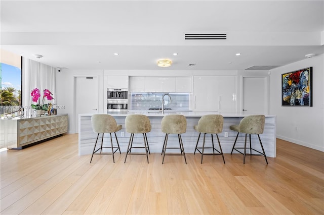 kitchen with white cabinets, a breakfast bar, and light hardwood / wood-style flooring