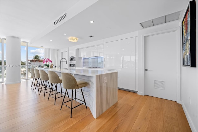 kitchen with sink, light hardwood / wood-style flooring, a breakfast bar area, a kitchen island with sink, and white cabinets