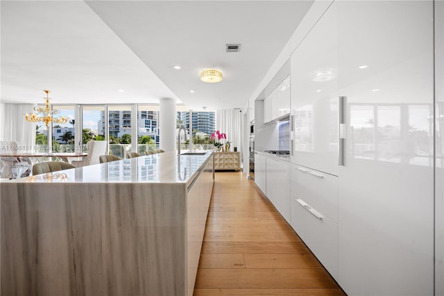 kitchen featuring white cabinetry, sink, pendant lighting, a spacious island, and light hardwood / wood-style floors