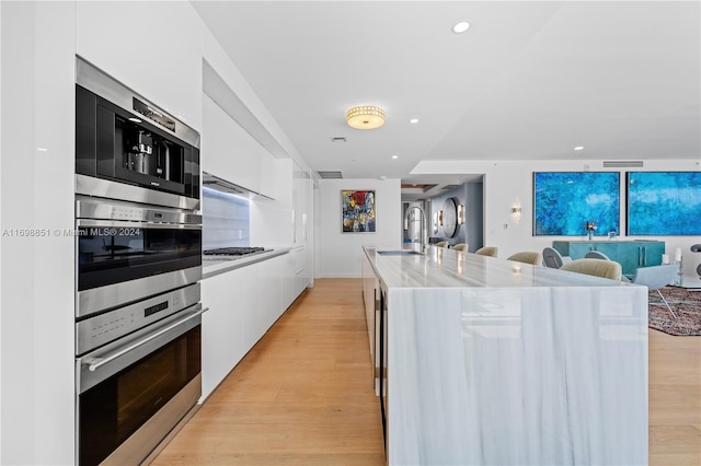 kitchen featuring white cabinetry, an island with sink, stainless steel appliances, and light hardwood / wood-style floors