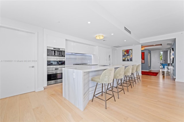 kitchen with white cabinetry, stainless steel appliances, an island with sink, a breakfast bar, and light wood-type flooring