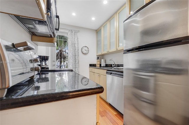 kitchen with dark stone counters, stainless steel appliances, light hardwood / wood-style floors, and sink