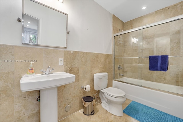 bathroom featuring combined bath / shower with glass door, tile patterned flooring, toilet, and tile walls