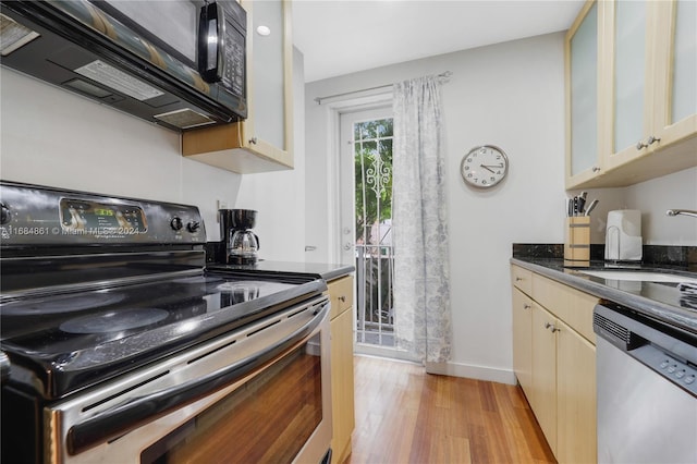 kitchen featuring dark stone counters, black appliances, sink, cream cabinetry, and light hardwood / wood-style floors