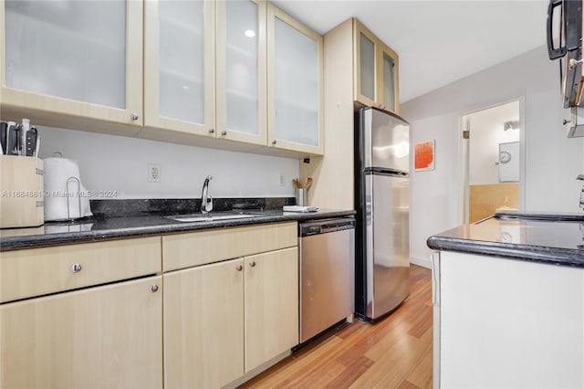 kitchen featuring appliances with stainless steel finishes, light wood-type flooring, dark stone countertops, and sink