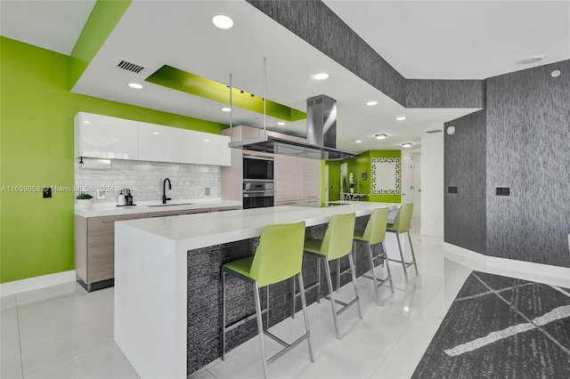 kitchen with white cabinets, a breakfast bar, a spacious island, and sink