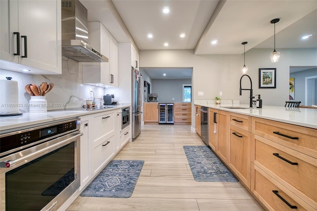 kitchen with sink, wall chimney exhaust hood, stainless steel appliances, decorative light fixtures, and white cabinets